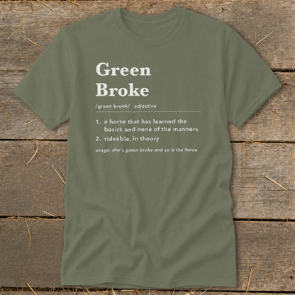 An olive green t-shirt with white text defining the adjective "Green Broke" on a wooden background.