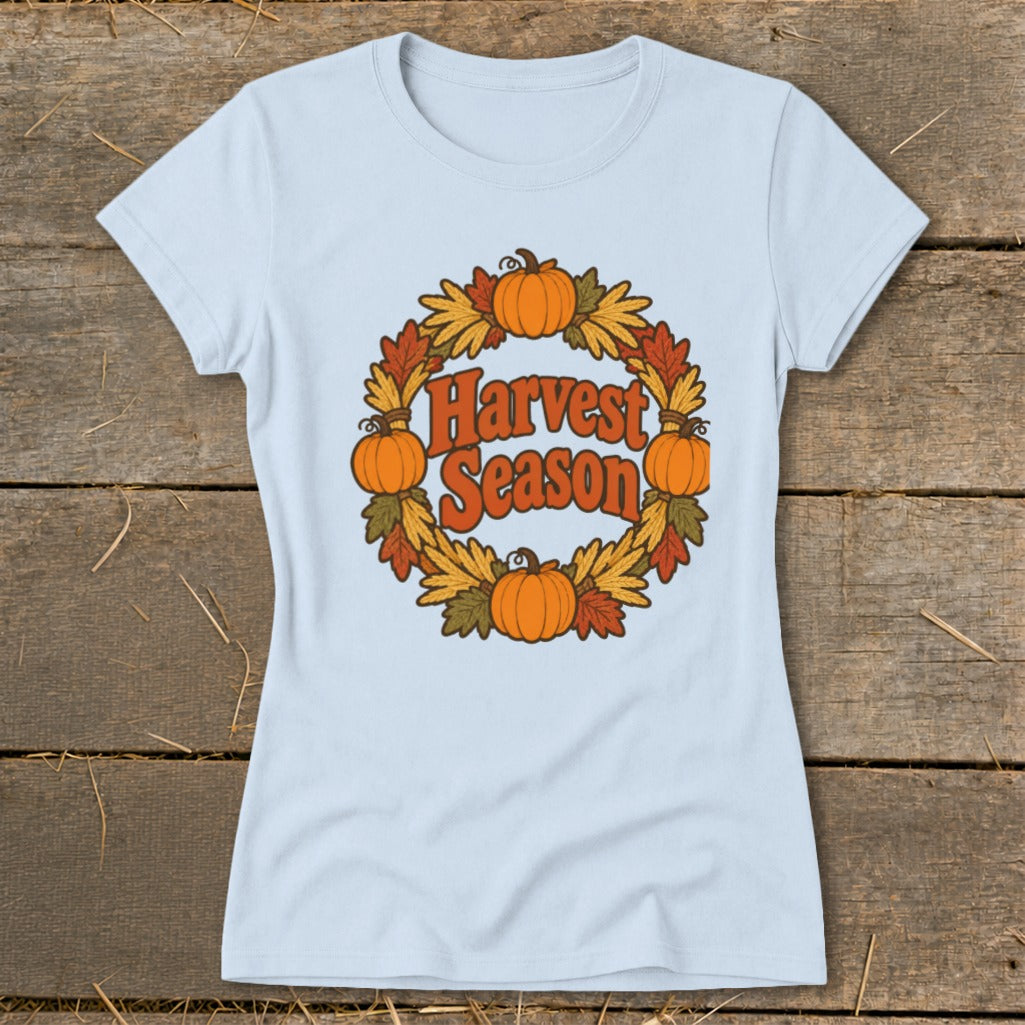 Light blue t-shirt with a circular harvest wreath design featuring pumpkins and autumn leaves with "Harvest Season" text.
