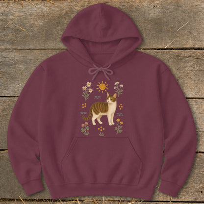 Maroon hoodie with a tabby cat illustration surrounded by flowers, sun, and waves.