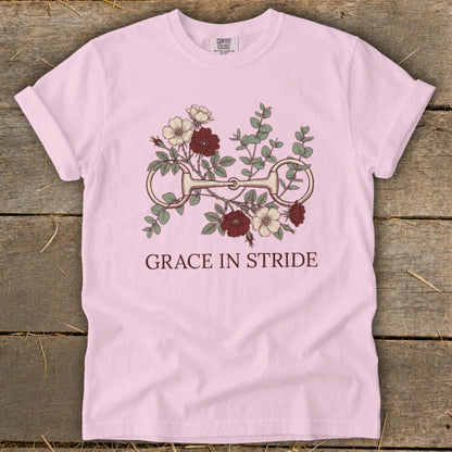 Pink t-shirt with floral design featuring a horse bit and text "GRACE IN STRIDE."