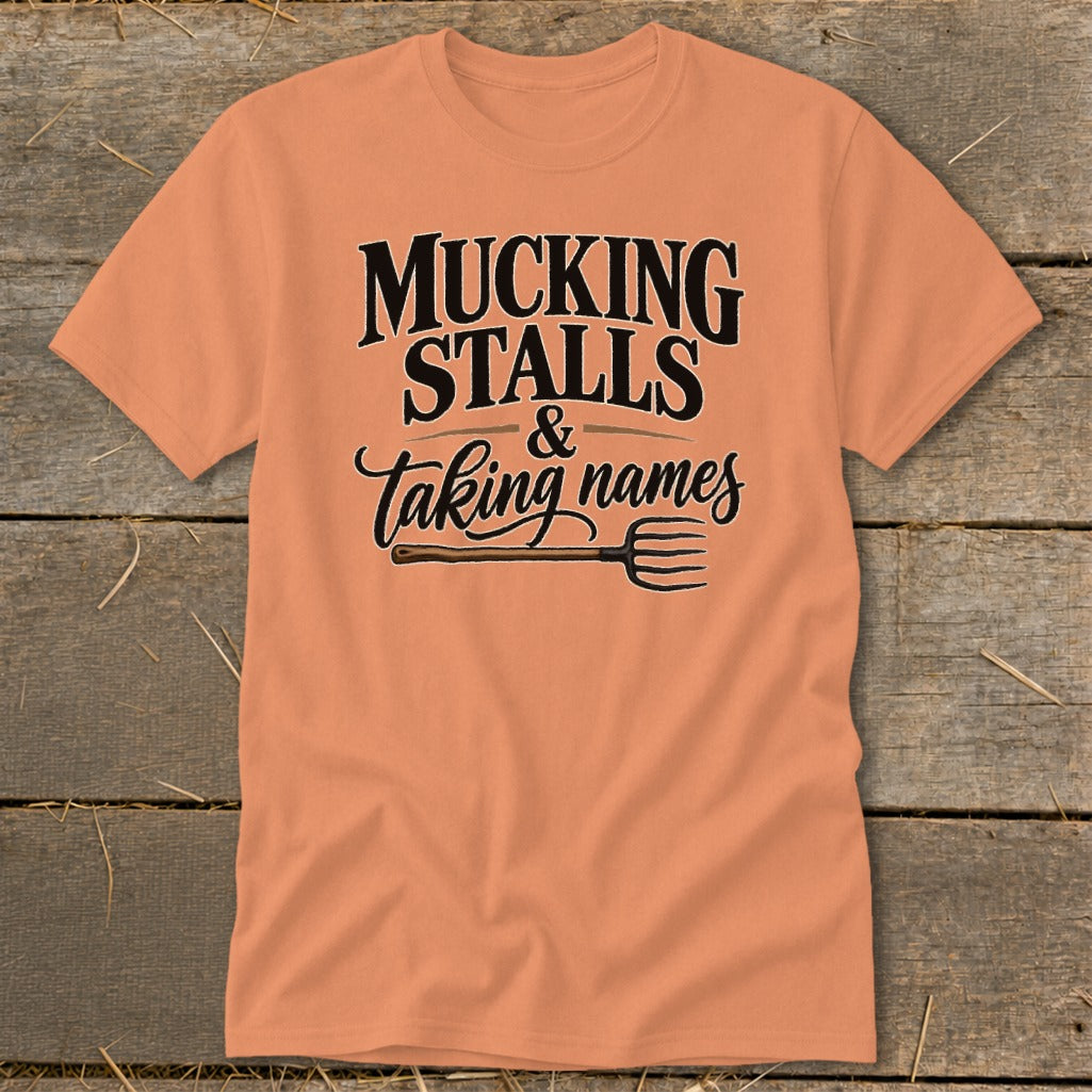 Orange t-shirt with text "MUCKING STALLS & Taking names" and a pitchfork.