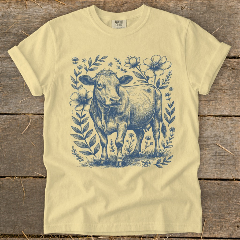 Yellow t-shirt with a blue sketch of a cow surrounded by flowers and leaves.