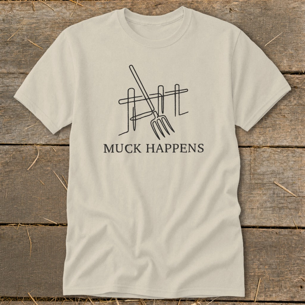 Beige t-shirt with line art of a pitchfork leaning against a fence and the text "MUCK HAPPENS".