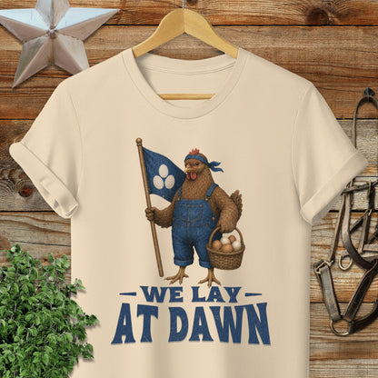 Cream t-shirt with chicken in overalls holding flag and basket, reads "We Lay At Dawn".