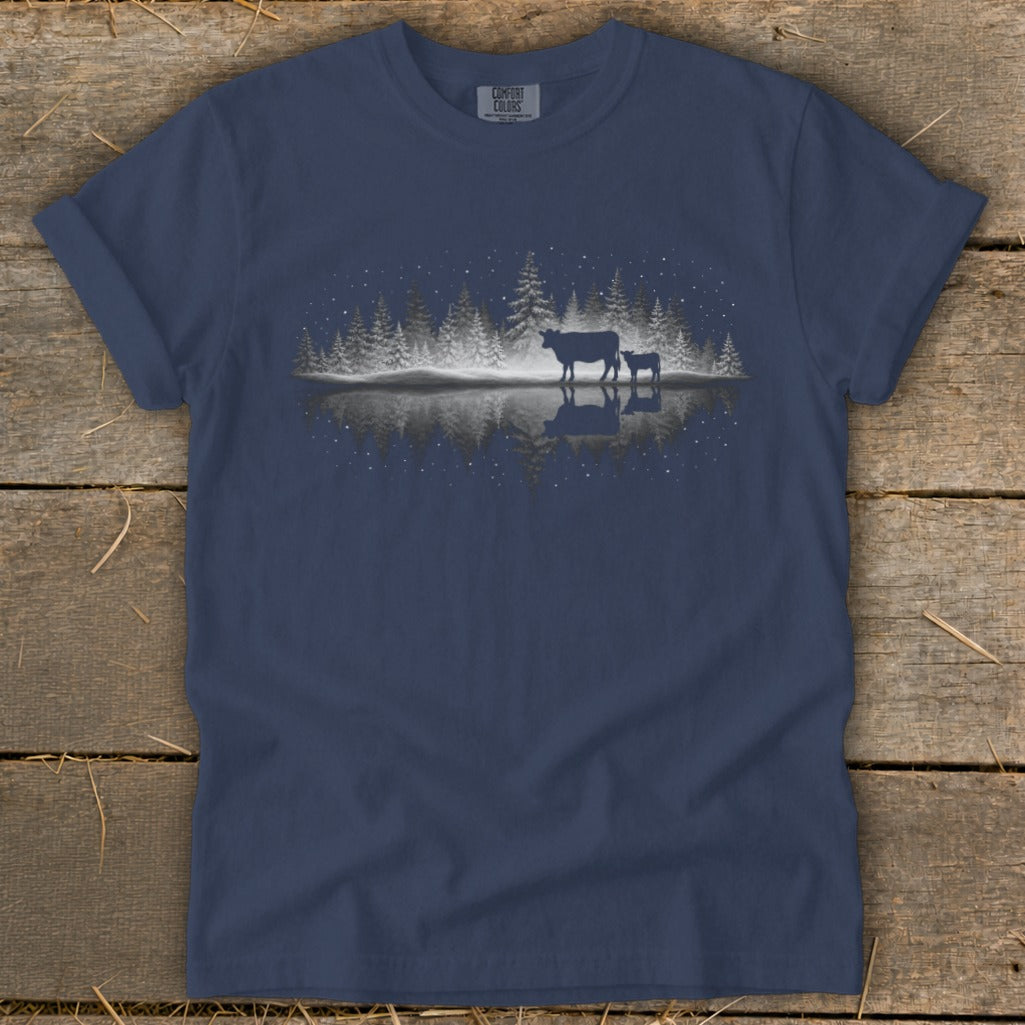 Cow and calf silhouette with snowy trees reflected in water at night.