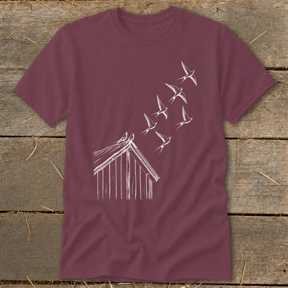 Maroon short-sleeved t-shirt featuring a white line drawing of a barn and flock of flying swallows.