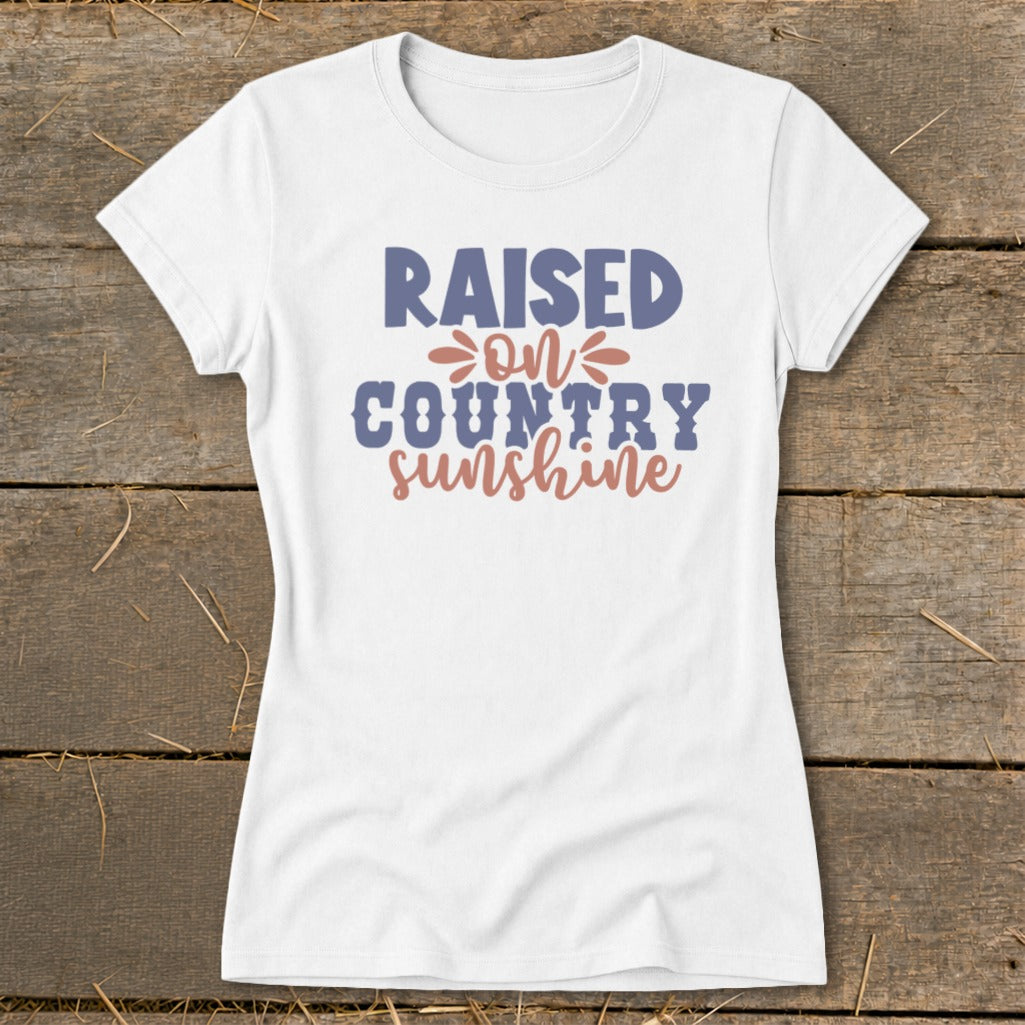 White t-shirt with text "RAISED ON COUNTRY sunshine" in blue and pink.