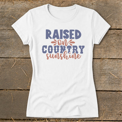White t-shirt with text "RAISED ON COUNTRY sunshine" in blue and pink.