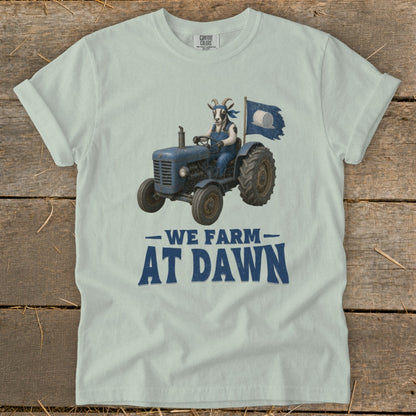 Light blue t-shirt with a goat driving a tractor and the text "WE FARM AT DAWN".