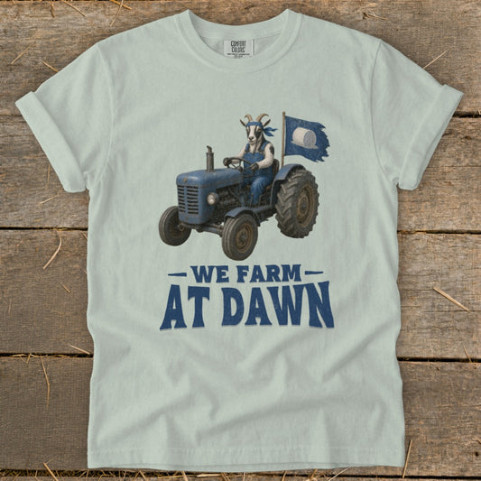 Light blue t-shirt with a goat driving a tractor and the text "WE FARM AT DAWN".