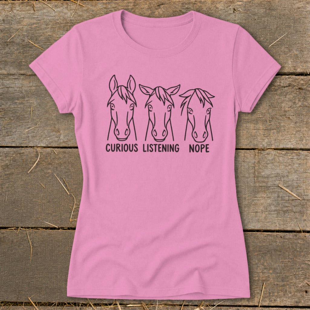 Pink short-sleeved t-shirt featuring line art of three horse heads with the text curious listening nope.
