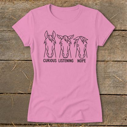 Pink short-sleeved t-shirt featuring line art of three horse heads with the text curious listening nope.