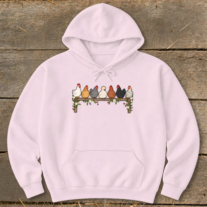 Light pink hoodie featuring a graphic of seven colorful chickens perched on a flower-covered fence.