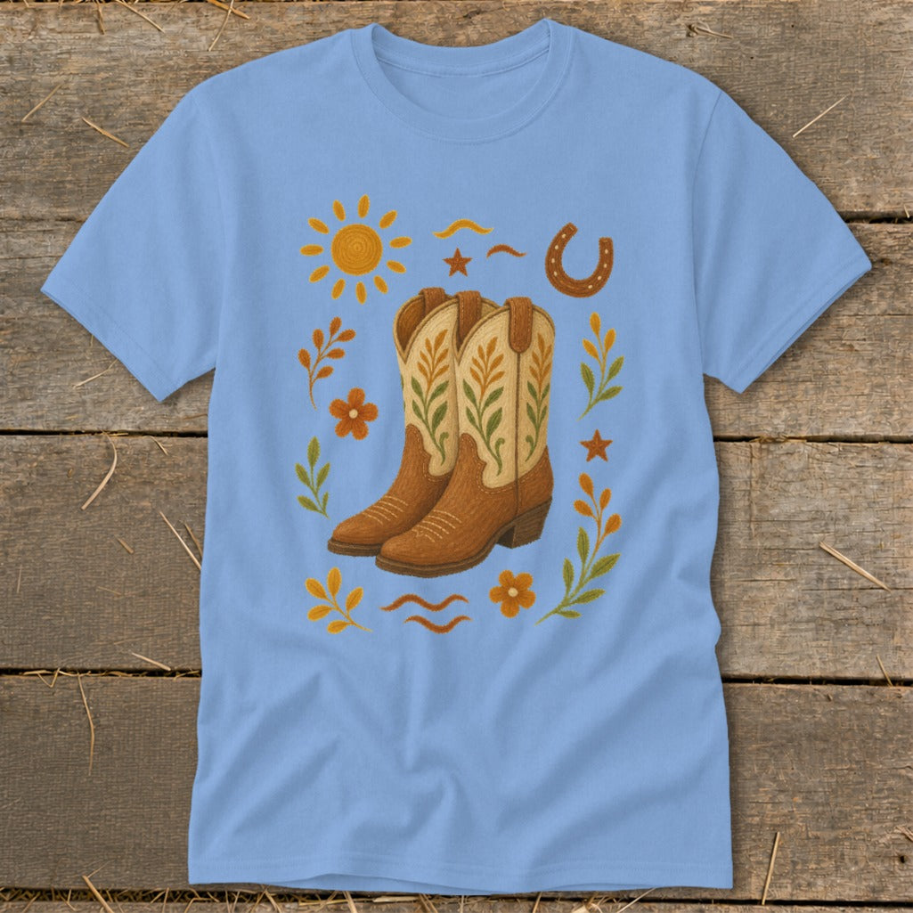 Light blue t-shirt with cowboy boots, sun, horseshoe, flowers, and leaves graphic.