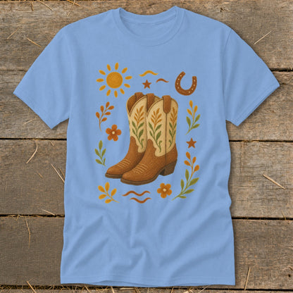 Light blue t-shirt with cowboy boots, sun, horseshoe, flowers, and leaves graphic.