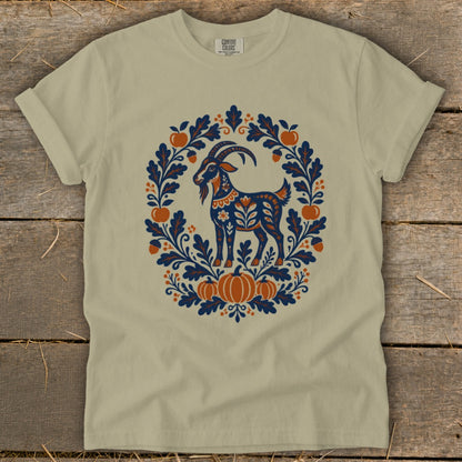 Olive green short-sleeve t-shirt featuring a folk-art graphic of a goat surrounded by an autumn wreath of leaves, acorns, apples, and pumpkins.