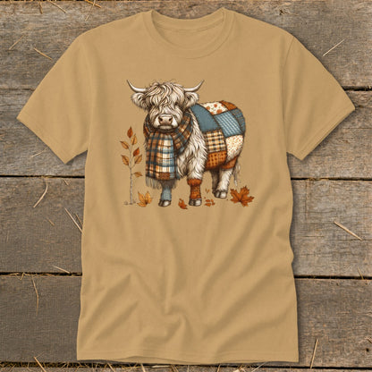 Fluffy Highland cow wearing a plaid scarf and patchwork blanket, with autumn leaves.
