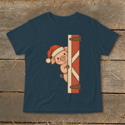 Christmas pig peeking from behind a red barn door on a navy blue t-shirt.