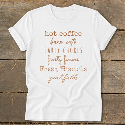 White t-shirt with brown text listing "hot coffee, barn cats, early chores, frosty fences, Fresh Biscuits, quiet fields".
