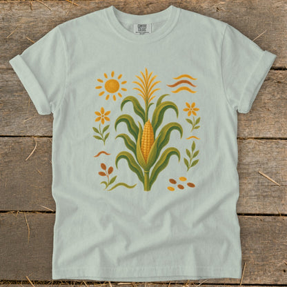 Light blue t-shirt with a corn stalk, sun, flowers, and seeds graphic.