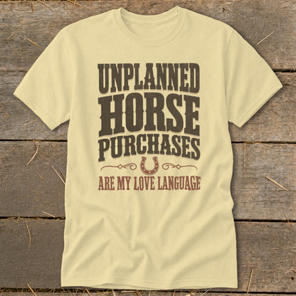 Light yellow t-shirt with brown text reading "Unplanned Horse Purchases Are My Love Language" and a horseshoe graphic.