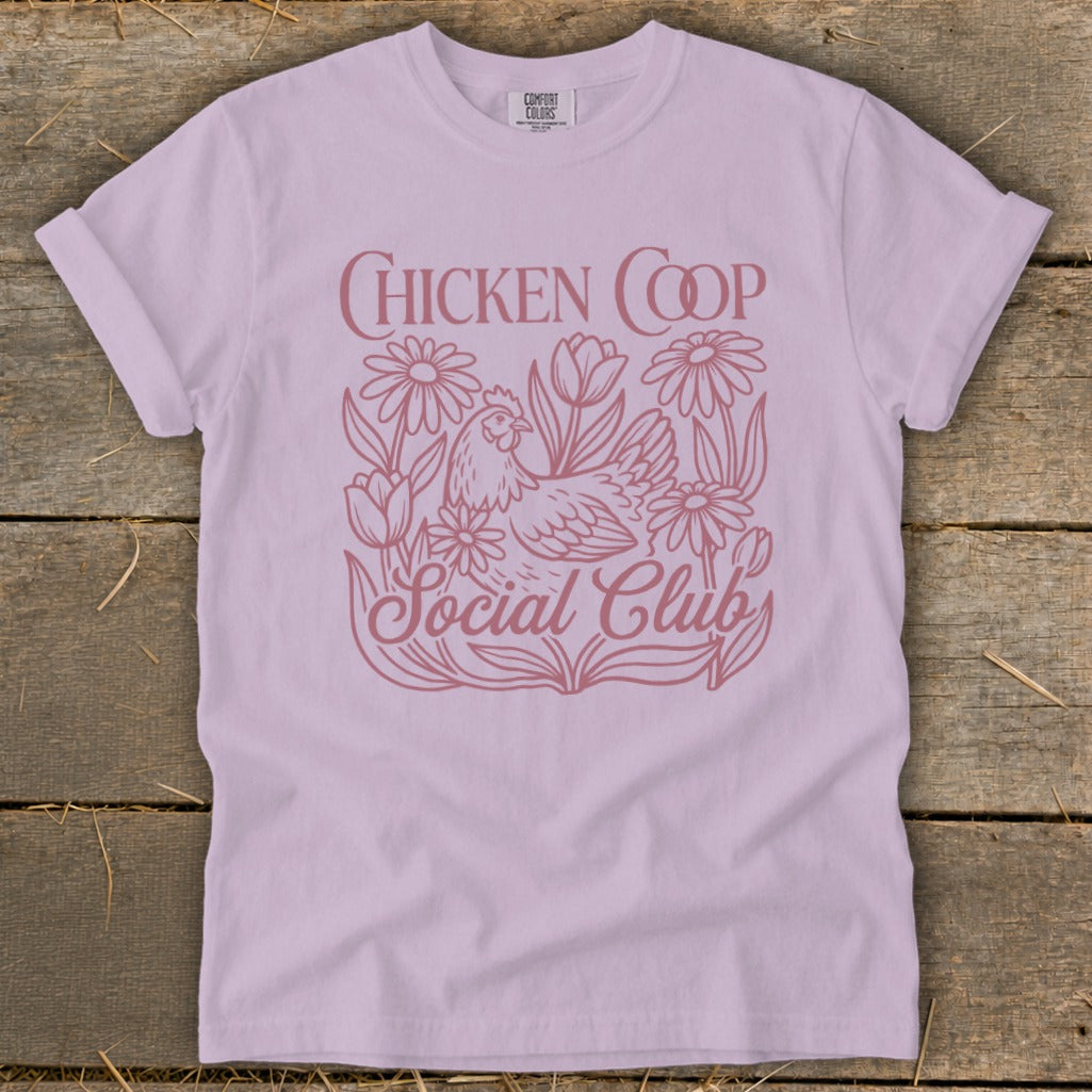 Lavender t-shirt with a pink line drawing of a chicken among flowers and text "CHICKEN COOP Social Club".