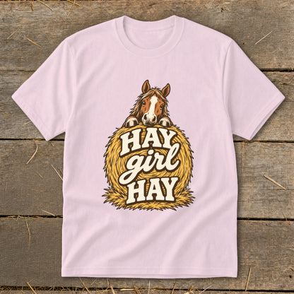 Light pink t-shirt with a horse peeking over a hay bale that says "Hay girl HAY".