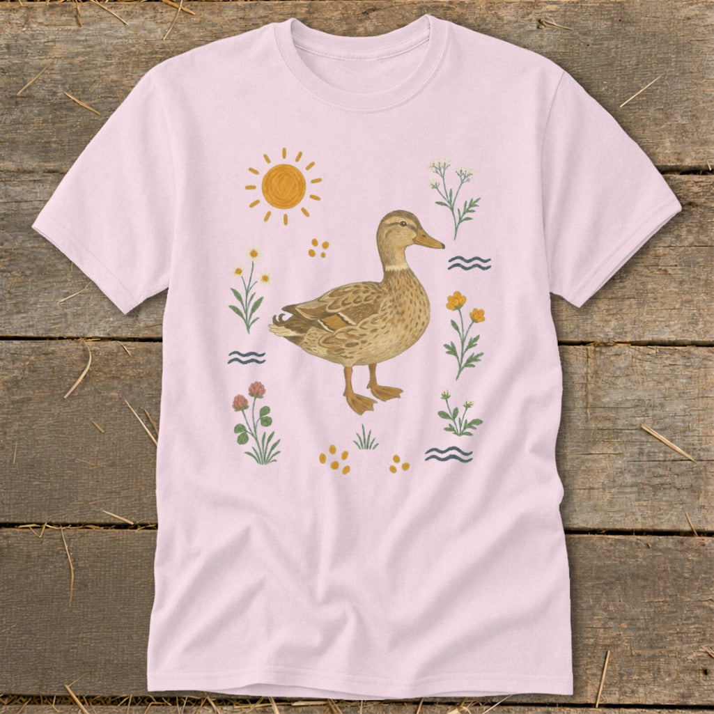 Pink t-shirt with a watercolor-style duck surrounded by flowers, sun, and water.