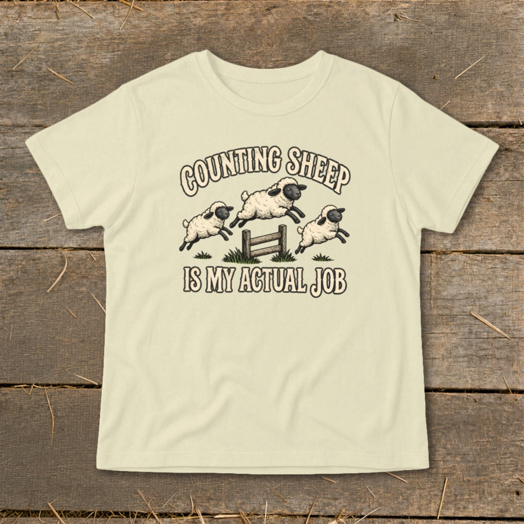 Light yellow t-shirt with "Counting Sheep Is My Actual Job" text and jumping sheep graphic.