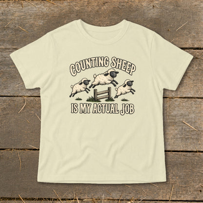 Light yellow t-shirt with "Counting Sheep Is My Actual Job" text and jumping sheep graphic.