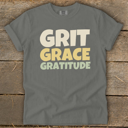 A gray t-shirt with the words Grit, Grace, and Gratitude printed across the chest in stacked block letters.