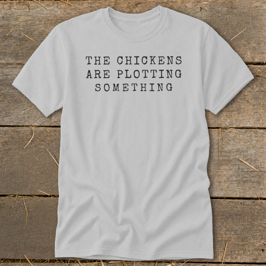 Light gray t-shirt with black text: "THE CHICKENS ARE PLOTTING SOMETHING".