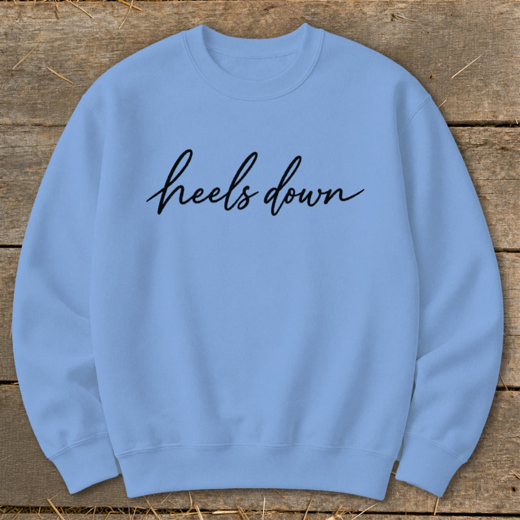 Light blue crewneck sweatshirt with black script text "heels down".