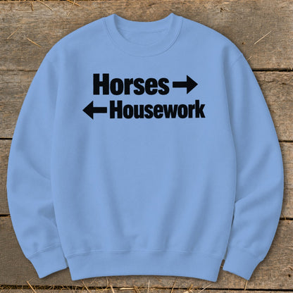A light blue crewneck sweatshirt featuring black text that reads Horses with a right arrow and Housework with a left arrow.