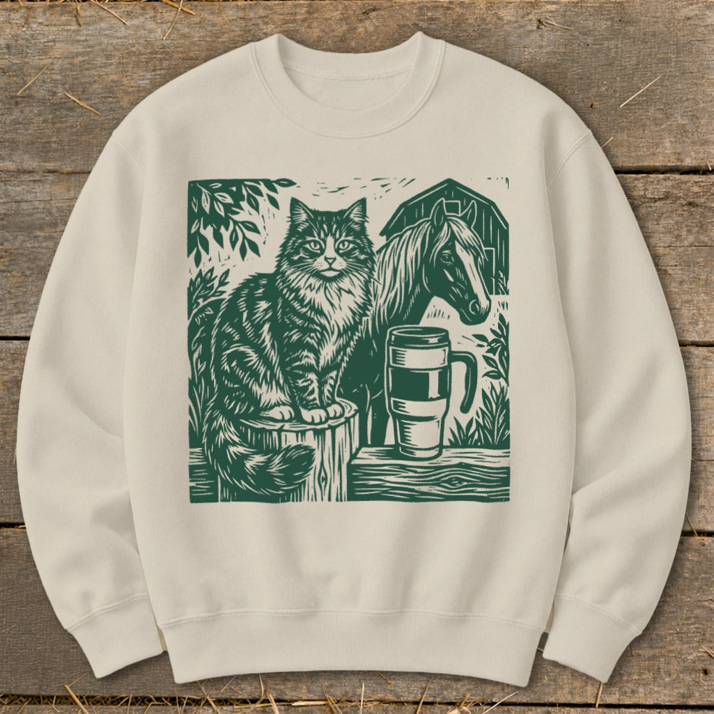 Cream sweatshirt with green linocut print of a cat, horse, mug, and barn.