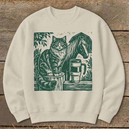 Cream sweatshirt with green linocut print of a cat, horse, mug, and barn.