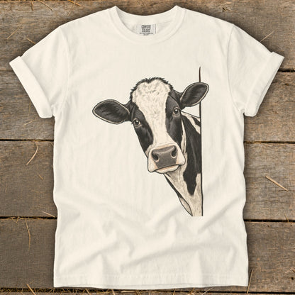 Cream t-shirt with a black and white cow peeking from the side.