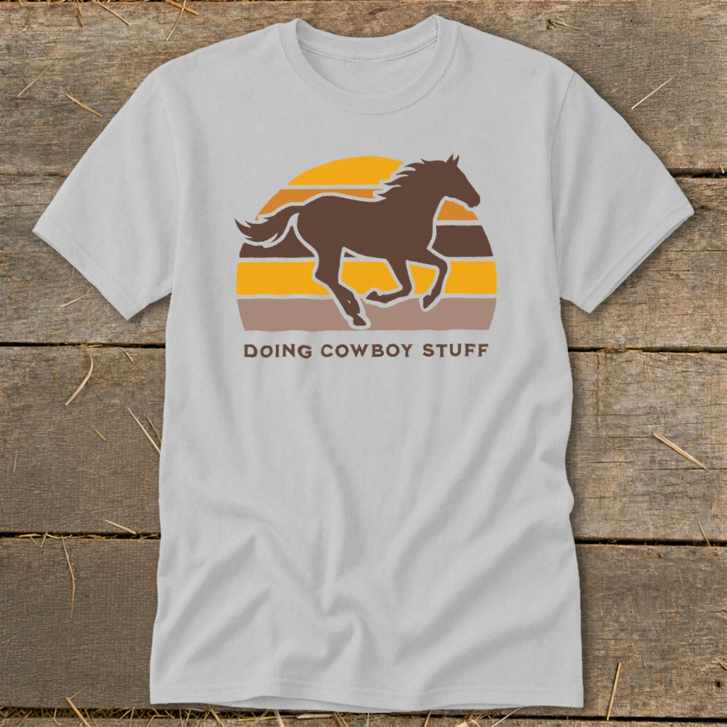 Light grey t-shirt with a brown horse silhouette running against a sunset with text "DOING COWBOY STUFF".