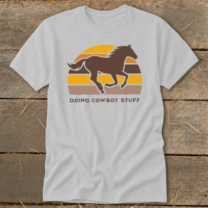 Light grey t-shirt with a brown horse silhouette running against a sunset with text "DOING COWBOY STUFF".