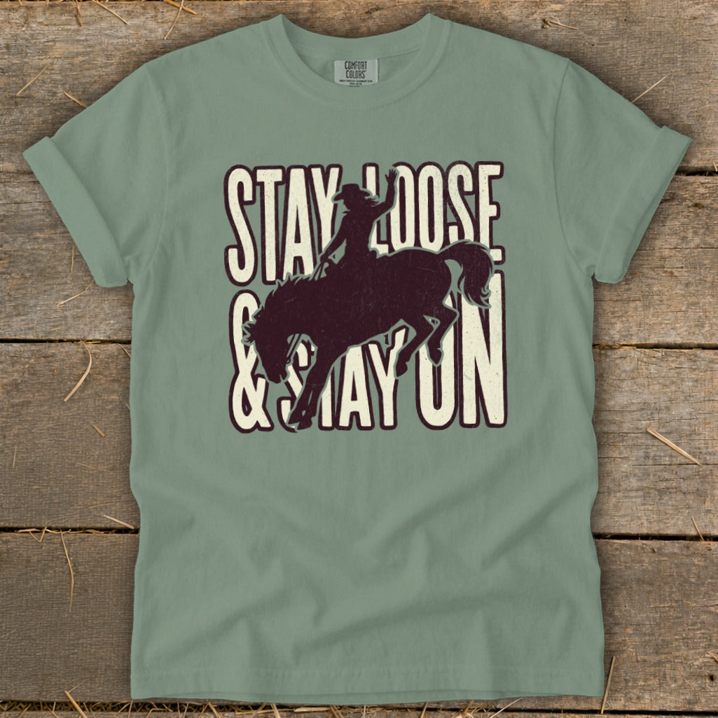 Sage green t-shirt with "STAY LOOSE & STAY ON" and bucking bronco graphic.