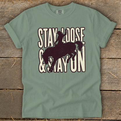 Sage green t-shirt with "STAY LOOSE & STAY ON" and bucking bronco graphic.