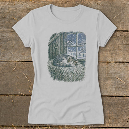 T-shirt graphic of a sleeping cat on hay in front of a snowy barn window.
