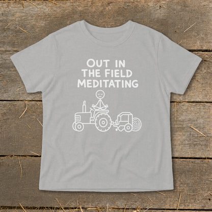 Gray t-shirt with white text "OUT IN THE FIELD MEDITATING" above a tractor with a meditating stick figure.