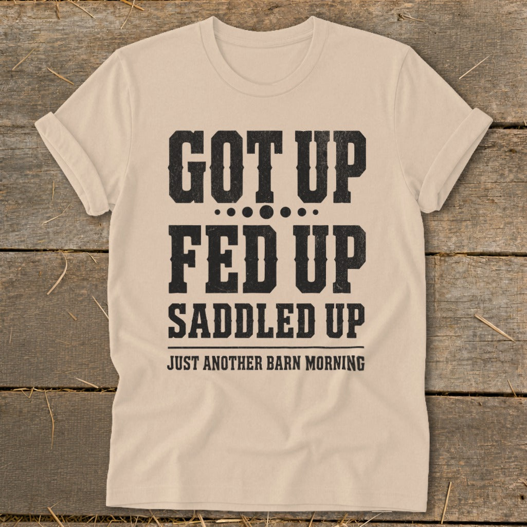 Tan t-shirt with black text: "Got Up, Fed Up, Saddled Up, Just Another Barn Morning."