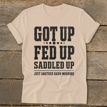 Tan t-shirt with black text: "Got Up, Fed Up, Saddled Up, Just Another Barn Morning."