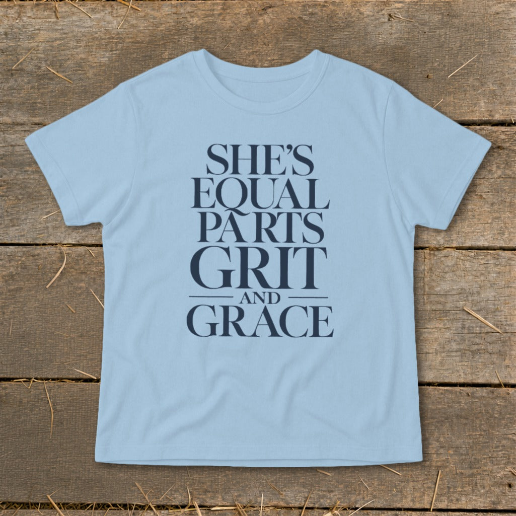 Light blue t-shirt with navy text "SHE'S EQUAL PARTS GRIT AND GRACE".