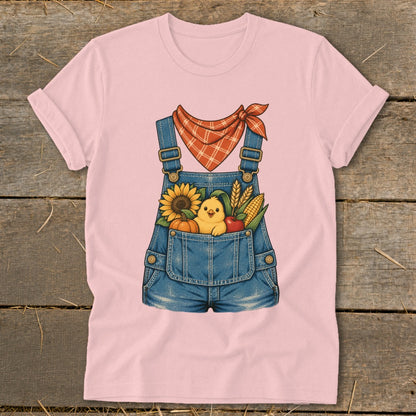 Pink t-shirt with illustration of denim overalls filled with a chick, sunflower, pumpkin, corn, and apple.