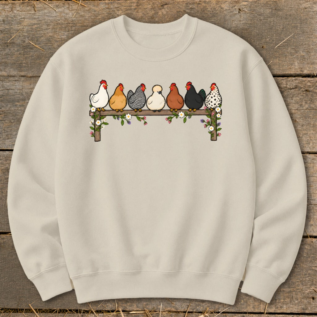 Light beige crewneck sweatshirt printed with seven colorful chickens sitting on a flower-covered wooden fence.