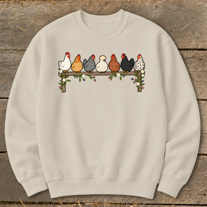 Light beige crewneck sweatshirt printed with seven colorful chickens sitting on a flower-covered wooden fence.