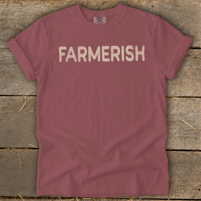 Maroon t-shirt with "FARMERISH" text in cream letters, on rustic wood background.